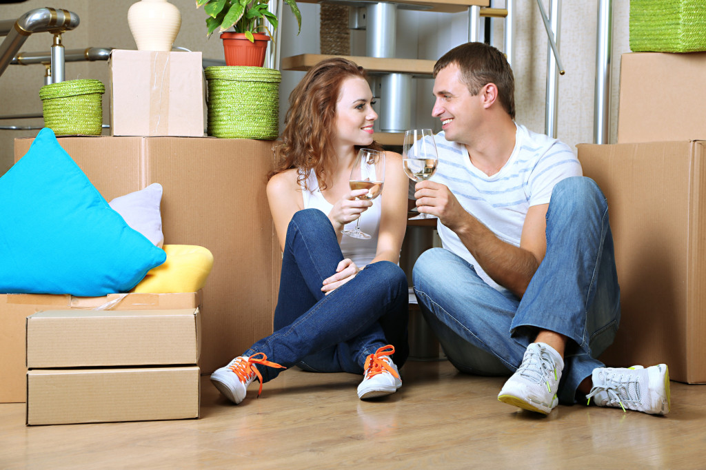 Young couple celebrating moving to new home sitting among boxes